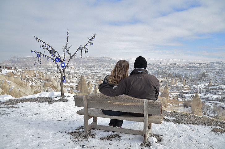 photo of couple sitting on brown bench while staring at the horizon