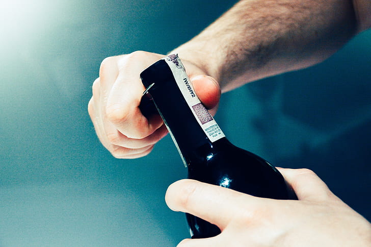 person opening black glass bottle