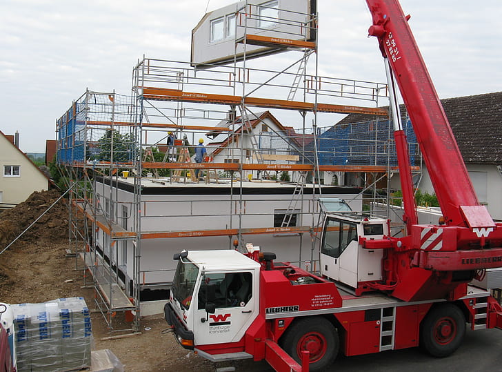 red and white crane truck lifting white building frame