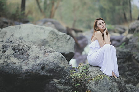 woman wearing white strapless dress sitting on the stone