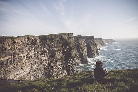 person sitting on cliff near ocean during daytime