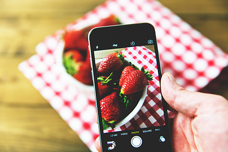 Man taking a photo of fresh strawberry fruit on his mobile iPhone smartphone