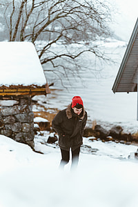 man in brown fur-trim hooded jacket wearing red knit cap walking on snow-terrain during daytime