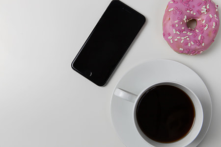 Coffee cup, iPhone mobile smartphone and donut on white desk