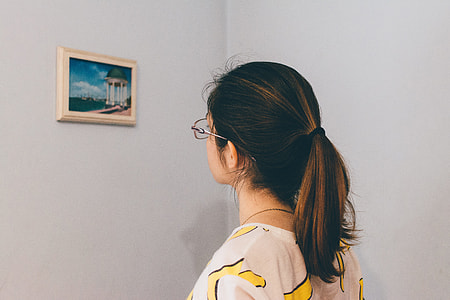 woman in eyeglasses standing and staring at the painting on the wall