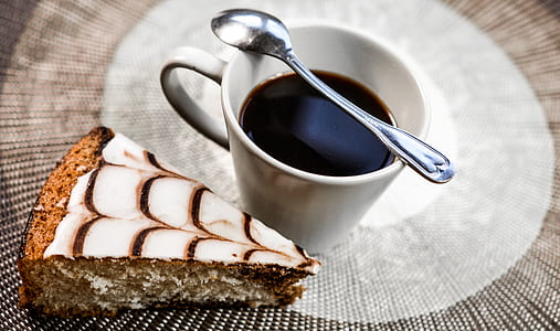 slice of cake beside cup of coffee with spoon