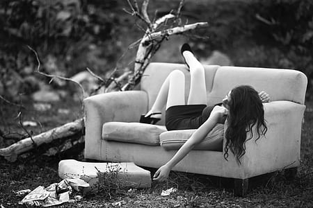 grayscale photography of woman wearing dress lying on 2-seated sofa