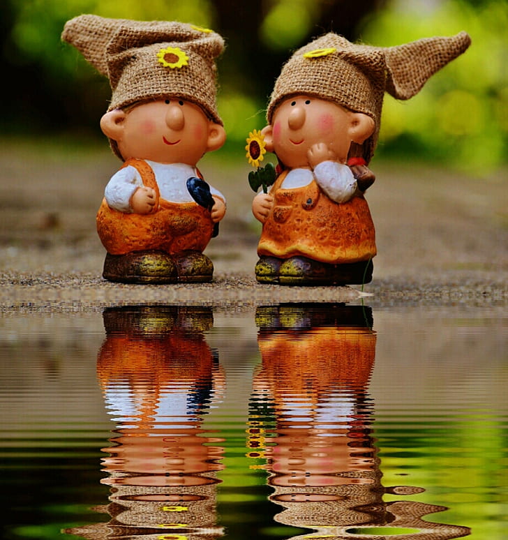Girl and Boy Figurines Facing Each Other Near Body of Water