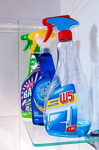 three cleaning spray bottles on top of glass-top wall shelf