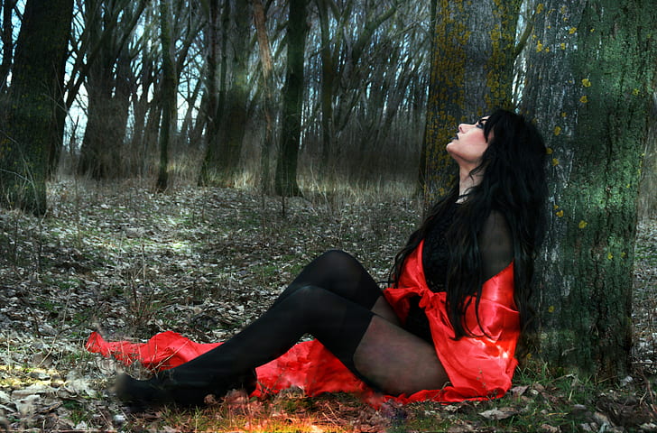 woman wearing red and black mesh bodysuit sitting beside tree