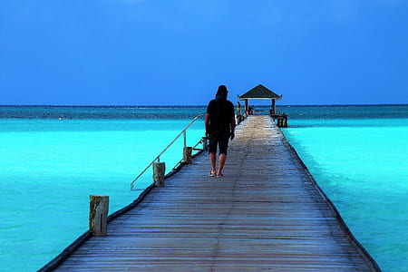 man walking on brown walking dock above calm water at daytime