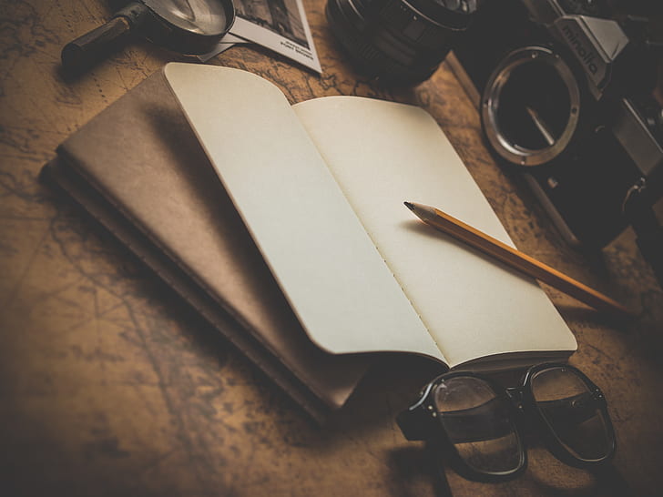 pencil, black framed eyeglasses, book, camera, and magnifying glass on brown surface