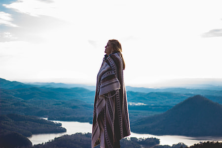 women's wearing brown and white blanket standing on top of the mountain