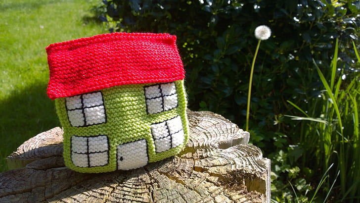 green and red knit miniature house on brown wood slab near green plants at daytime