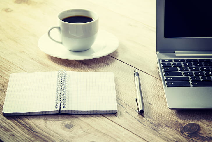 white cup and saucer beside gray laptop computer