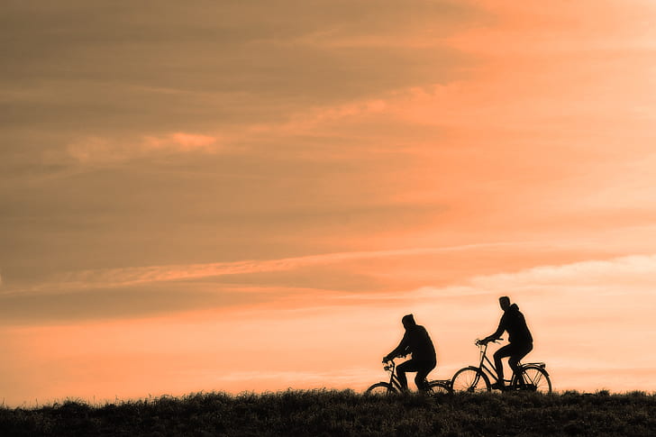 two silhouette of man riding bicycle during golden hour time