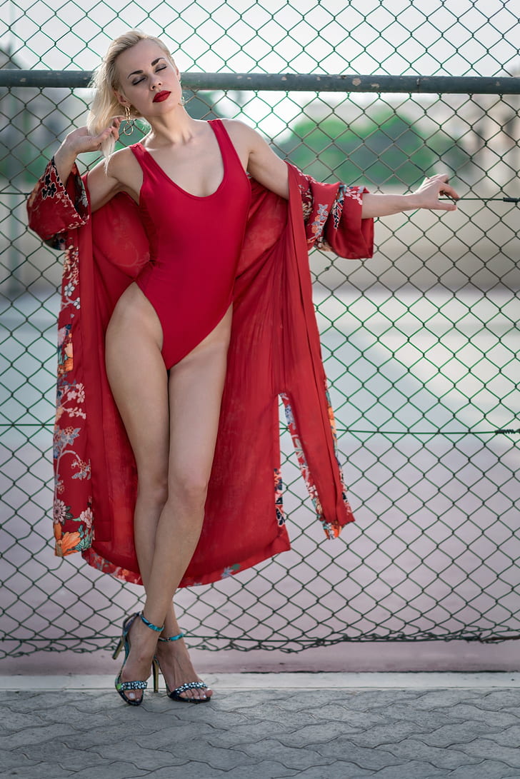 woman wearing red one-piece swimwear with red floral robe near gray metal fence