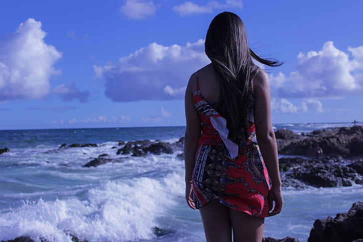 woman in red mini dress standing near sea during daytime