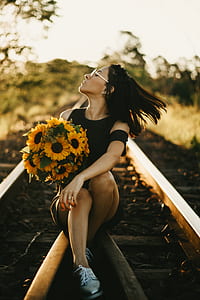 woman in black off-shoulder top holding bouquet of sunflowers