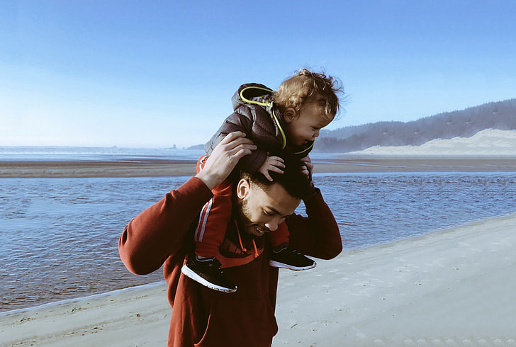 man carrying toddler on her back near body of water