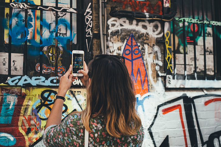 woman in black floral shirt holding silver iPhone 6 taking picture of graffiti
