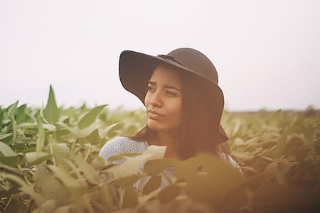 woman with black hat and white top between green plant under white sky during daytime