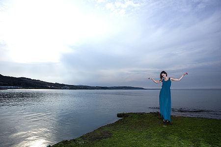 woman in blue long dress standing beside the body of water