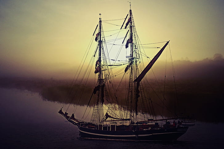 black galleon on body of water during sunset