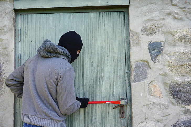 man wearing grey zip-up jacket holding red hand tool beside door