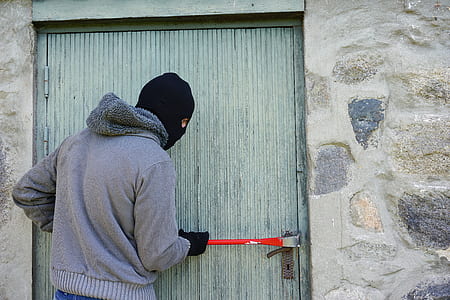 man wearing grey zip-up jacket holding red hand tool beside door
