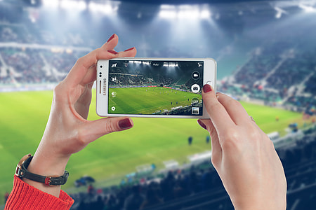 Woman photographer taking photo with mobile smartphone in stadium of soccer match