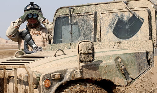 soldier wearing vest holding binoculars standing beside truck