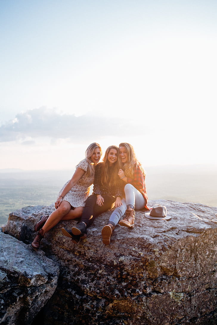 three women sitting on gray rock