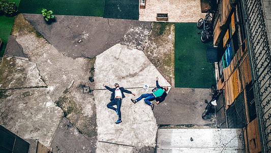 aerial photo of two men lying at white and gray concrete floor in front of brown building during daytime
