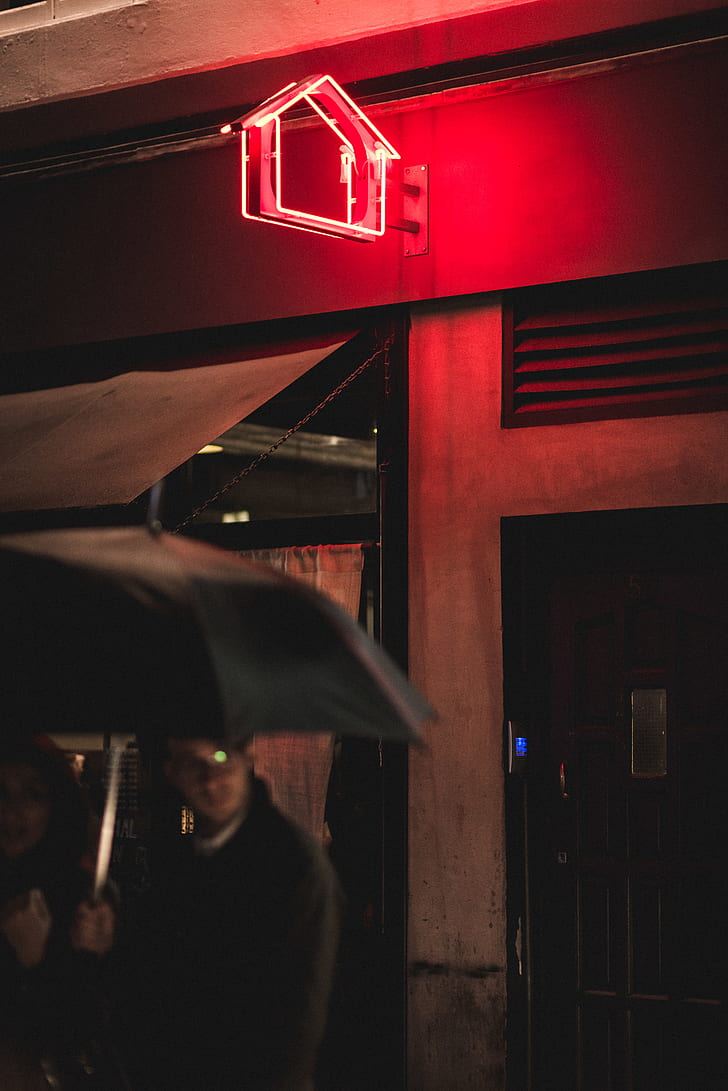 man and woman holding black umbrella near red neon light signage