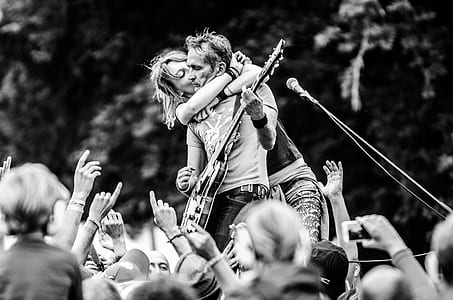 Grayscale Photo of a Woman Kissing a Man Playing Guitar