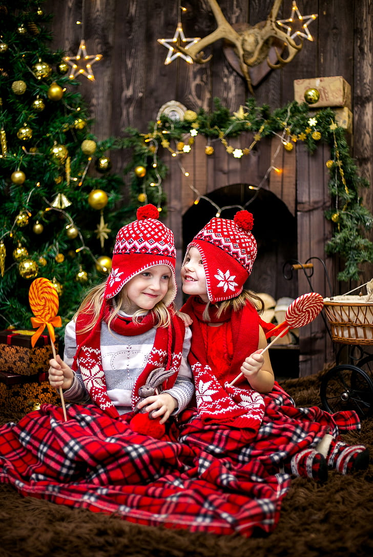 two girls in red-white-and-black fair isle ear-flap hat and scarfs holding lollipops