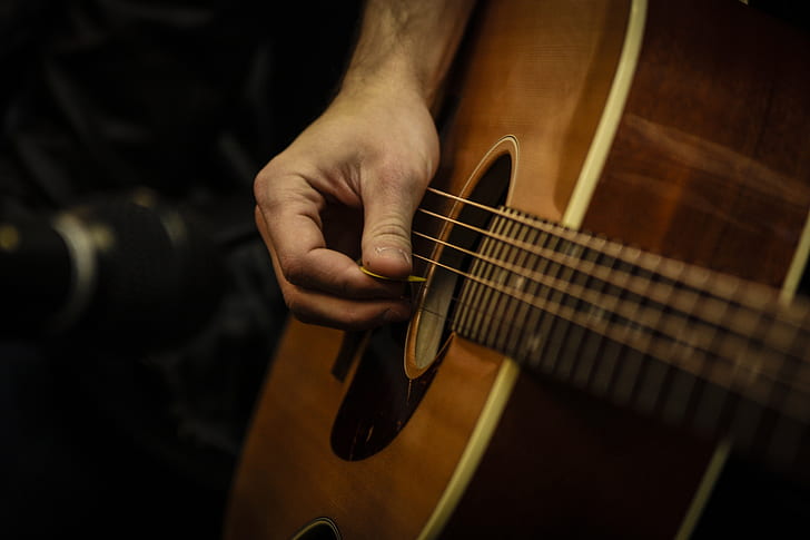 photo of person holding using pick on guitar