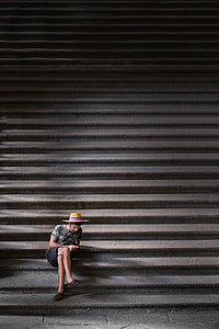 photo of man in brown wicker hat, gray T-shirt, and black shorts sitting on staircase