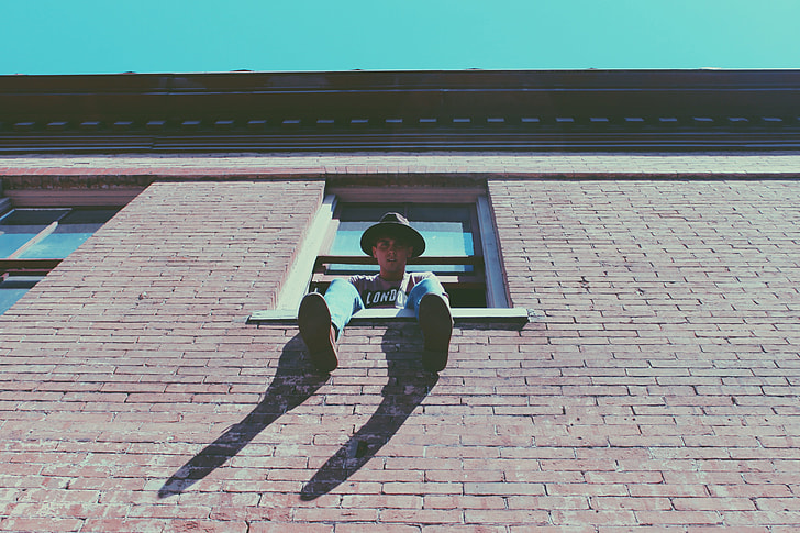 man sitting on window during daytime