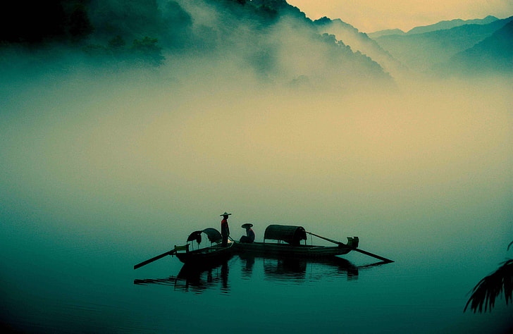 silhouette of people on wooden paddle boats on foggy lake