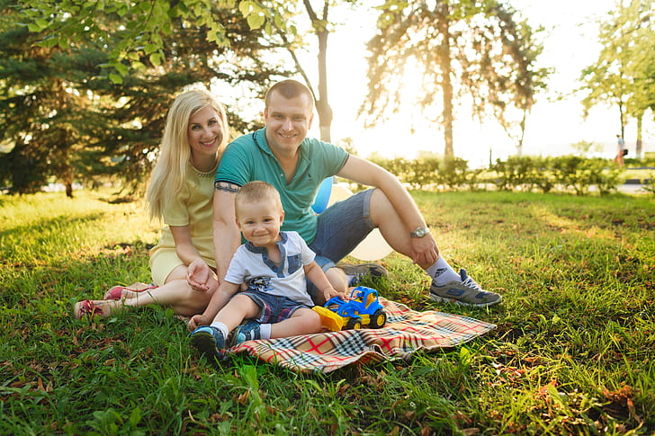 family of three sitting on the green grass