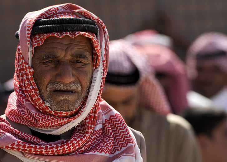 selective focus portrait photo of man in red keffiyeh with black agal headdress