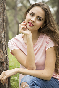 woman wearing pink shirt and blue denim bottoms sitting beside tree