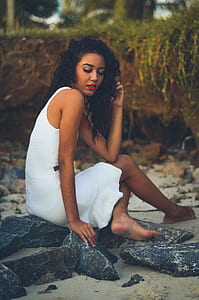 woman wearing white sleeveless mini dress sitting on rock