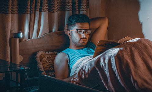 man reading book lying on bed