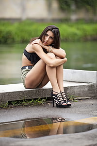 woman wearing black top and grey shorts sitting on concrete surface at daytime