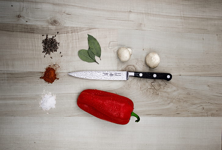 red bell peppers and gray kitchen knife on top of beige wood plank table