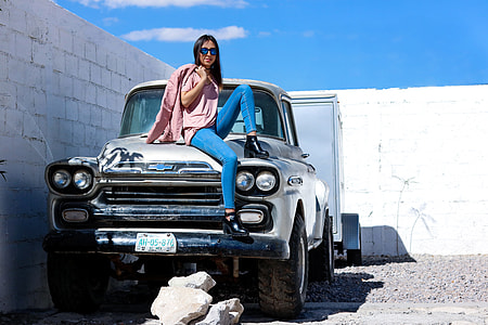 woman sitting on classic silver pickup truck beside white wall