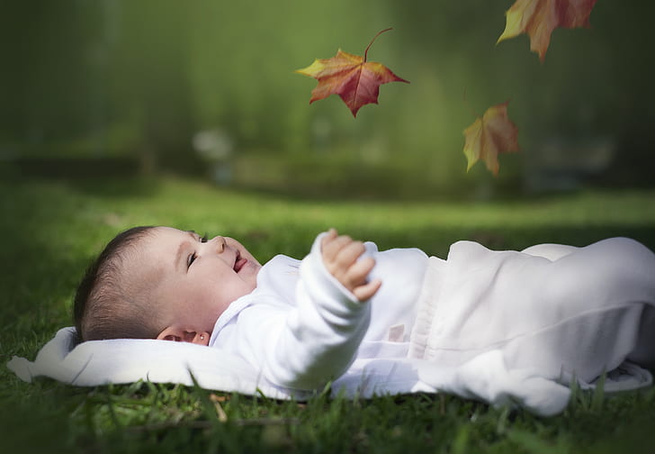 photograph of baby lying on grass with leaf smiling